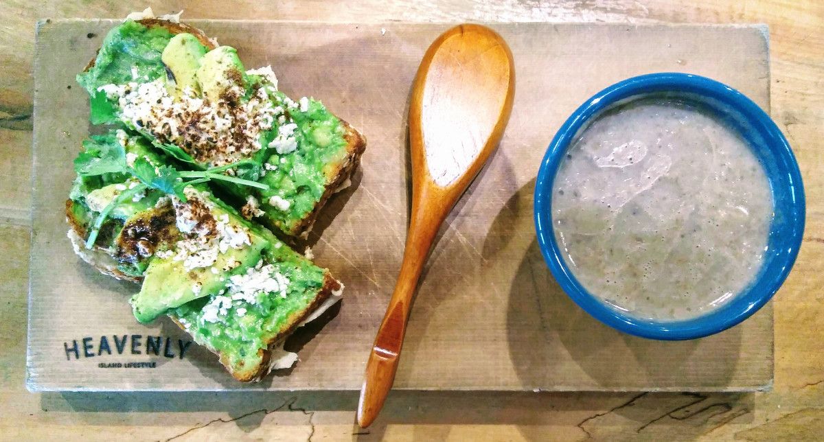 Avocado toast, wooden spoon, and bowl of soup on a wooden block.